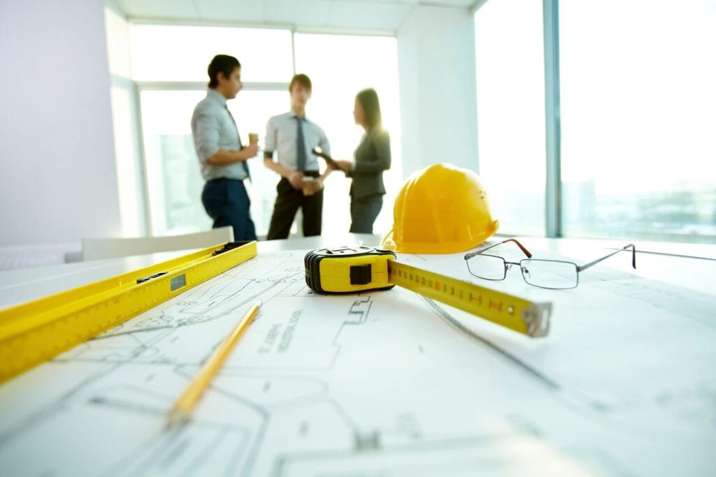 group of people having a discussion with a hard hat and enginnering tools in the foreground 